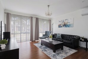 Una sala de estar moderna con un sofá de cuero negro, una mesita de centro y un televisor sobre un mueble negro.