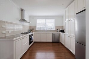 A kitchen with white cabinets, a stainless steel refrigerator, a window with blinds, and a tiled backsplash. - Havana Edge Pet friendly Garden Retreat near Beach (Frankston)