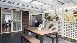 Una terrazza esterna con tavolo e panche in legno, un barbecue e vista sul giardino.