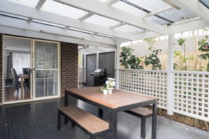 An outdoor patio with a wooden table and benches, a grill, and a view of the backyard. - Havana Edge Pet friendly Garden Retreat near Beach (Frankston)