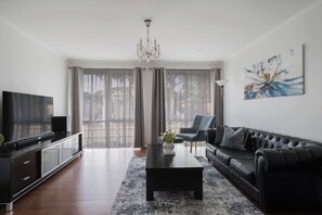 Un salon moderne avec un téléviseur à écran plat, un canapé en cuir noir, une table basse et un lustre.