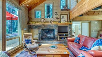 A cozy cabin interior with a stone fireplace, leather furniture, and large windows.