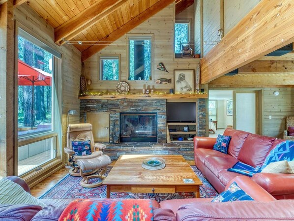 A cozy cabin interior with a stone fireplace, leather furniture, and large windows.