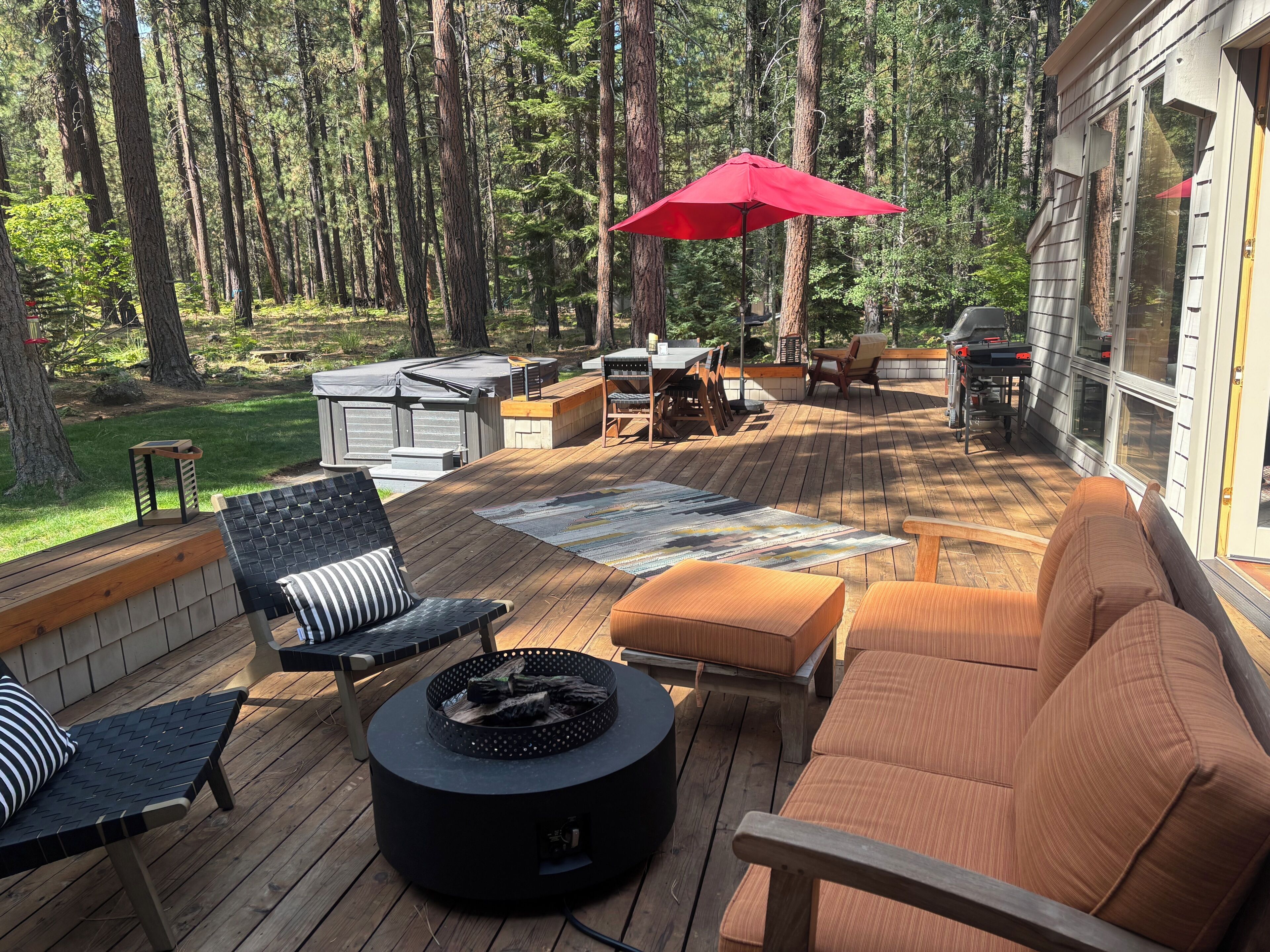 Une terrasse dotée de mobilier d’extérieur, d’un foyer et d’un parasol rouge.