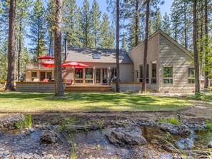 A two-story house with a covered patio and a stream in the foreground.