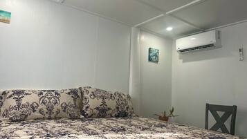A bedroom with a bed, a potted plant, an air conditioning unit, and a wall-mounted artwork.