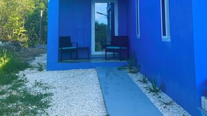 Una casa moderna con fachada azul, un patio cubierto con asientos y un camino de grava.