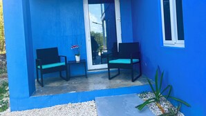 Fachada azul con dos sillas negras y una orquídea en maceta en un balcón.