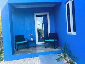A blue exterior with two black chairs and a potted orchid on a balcony.