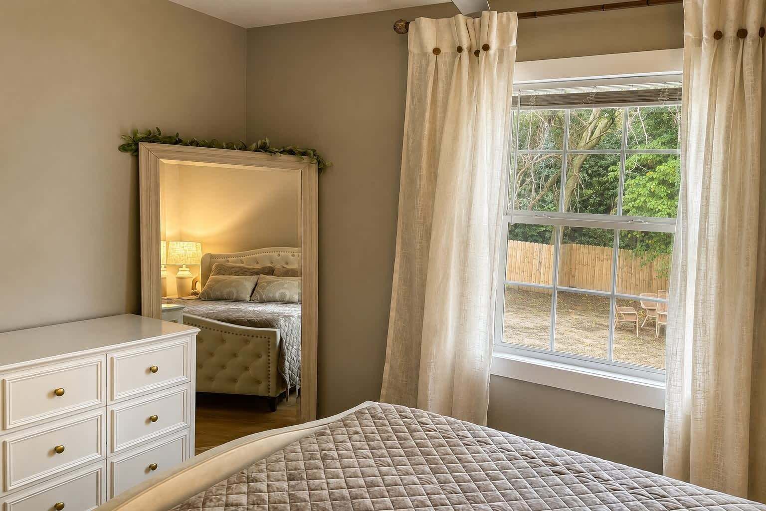 Una camera da letto con un letto, una cassettiera, uno specchio e una finestra con tende.