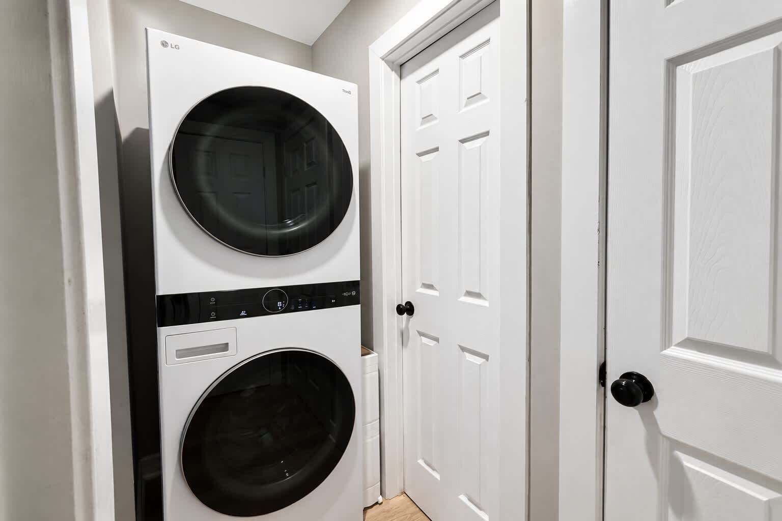 A laundry room with two stacked washing machines and a door.