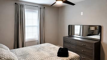A bedroom with a bed, a dresser, a ceiling fan, and a window with curtains.