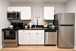 A modern kitchen with stainless steel appliances, white cabinetry, and a black countertop. - Downtown Duplex with Fenced Yard (Raleigh)