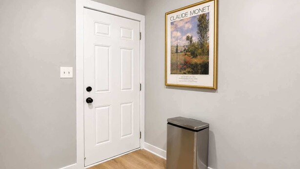 Een kamer met een witte deur, een vuilnisbak van roestvrij staal en een schilderij van Claude Monet aan de muur.