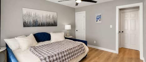 Un dormitorio con cama, ventilador de techo, mesita de noche, lámpara y puerta.