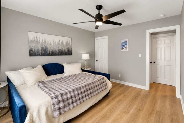 Une chambre à coucher avec un lit, un ventilateur de plafond, une table de chevet, une lampe et une porte.