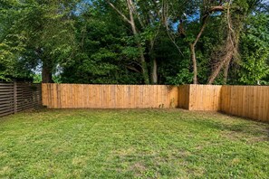 A fenced backyard with a grassy lawn and trees in the background. - Downtown Duplex with Fenced Yard (Raleigh)