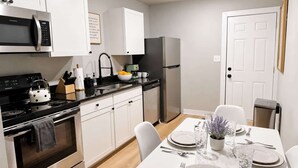 Une cuisine moderne avec des meubles blancs, une cuisinière noire, un réfrigérateur en acier inoxydable et une table à manger pour deux personnes.