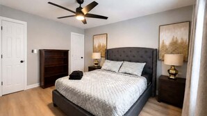 Une chambre à coucher avec un lit, des tables de chevet, un ventilateur de plafond et des œuvres d’art accrochées aux murs.