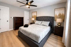 Ein Schlafzimmer mit einem Bett, Nachttischen, einem Deckenventilator und Kunstwerken an den Wänden.