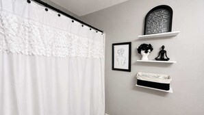 Une salle de bain avec un rideau de douche blanc, un dessin au trait encadré, une statue noire et un tableau noir avec des inscriptions.