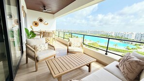 Ein Balkon mit Holzboden, Korbmöbeln und Blick auf ein Schwimmbad und Gebäude.