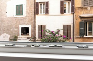 Une rangée de bâtiments aux fenêtres fermées par des volets et dotés d’un petit balcon orné de plantes en pot.