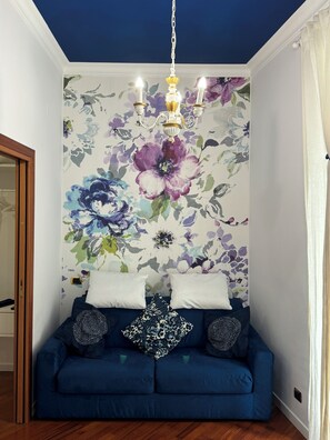 A room with a blue sofa, white cushions, and a floral wall mural. - Trastevere | Piazza Trilussa | Rome on Foot—Moro7— (Roma)