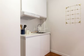 Eine kleine Küche mit weißen Schränken, einer Edelstahl-Spüle und einem an der Wand befestigten Wäscheständer.