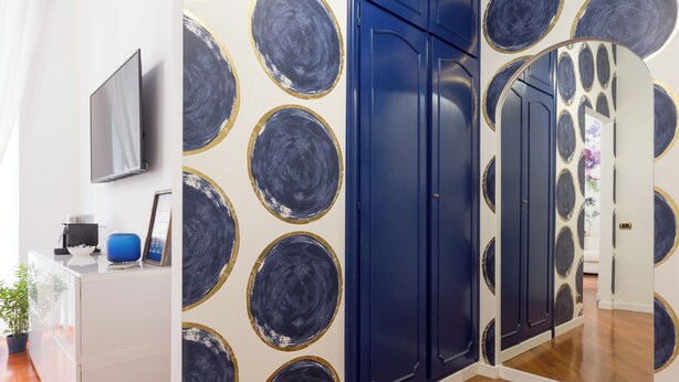 A room with a white desk, a flat-screen TV, and a blue chair. There are blue doors with gold trim and a mirror with a circular pattern. - Trastevere | Piazza Trilussa | Rome on Foot—Moro7— (Roma)