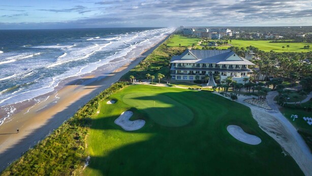 Ein Küsten-Golfplatz mit einem großen Gebäude, vermutlich eine Klubhaus, direkt neben dem Strand.