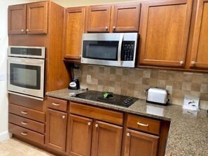 A kitchen with wooden cabinets, a microwave, an oven, a toaster, and a blender. - Pool-View 2BR Condo w/ Balcony & Resort Access (Palm Coast)