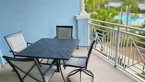 Ein Balkon mit Tisch und Stühlen, Blick auf einen Pool und eine blaue Wand.