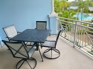 A balcony with a table and chairs, a view of a pool, and a blue wall. - Pool-View 2BR Condo w/ Balcony & Resort Access (Palm Coast)