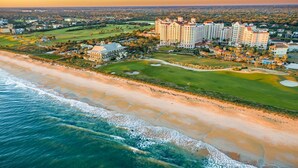 Vista aérea de um resort costeiro com propriedades na praia, um campo de golfe e um grande complexo hoteleiro.