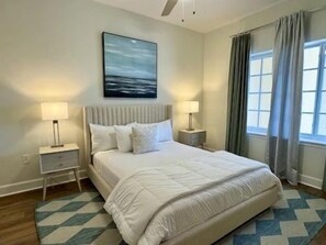 A bedroom with a bed, nightstands, a painting, and a window with curtains. - Harborview 2BR Condo | Hammock Beach Resort Access (Palm Coast)