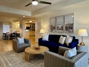 A living room with a blue sofa, two armchairs, a coffee table, and a dining area in the background. - Waterway-View 3BR Condo w/ Pool & Resort Access (Palm Coast)
