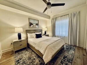 A bedroom with a bed, nightstands, a ceiling fan, a window with curtains, and a rug. - Waterway-View 3BR Condo w/ Pool & Resort Access (Palm Coast)