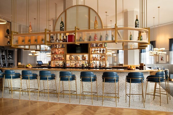 Angolo bar con un bancone curvo, numerose scaffalature piene di bottiglie e sgabelli da bar blu.