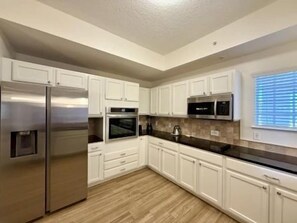 A kitchen with white cabinets, a stainless steel refrigerator, a microwave, and a black countertop. - Bright 3BR Condo w/ Hammock Beach Resort Access (Palm Coast)