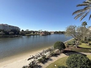 A lake with a sandy beach, a hotel in the background, and a well-maintained grassy area with trees. - Bright Waterfront 3BR Condo | Pool & Resort Access (Palm Coast)