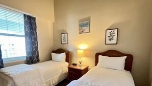 Une chambre d’hôtel avec deux lits simples, une table de chevet avec une lampe et une fenêtre avec des rideaux.