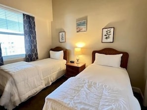 A hotel room with two single beds, a nightstand with a lamp, and a window with curtains. - Ocean & Golf View Condo w/ Pools & Resort Access (Palm Coast)