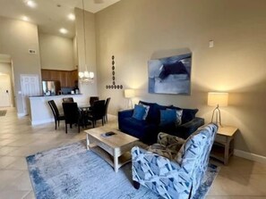 Un salon comprenant un canapé, une table basse, un fauteuil à motifs et un coin repas avec des chaises et une table.