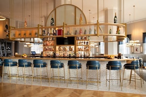 A bar area with a curved counter, multiple shelves of bottles, and blue bar stools. - Ocean-View 3BR Condo | Hammock Beach Resort Access (Palm Coast)