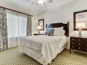 A hotel room with a bed, a nightstand, a dresser, a ceiling fan, and a window with curtains. - Waterway-View 2BR Condo w/ Pool + Resort Access (Palm Coast)