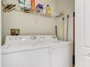 Un espace buanderie comprenant un lave-linge, un sèche-linge et une étagère où sont rangés les produits de nettoyage.