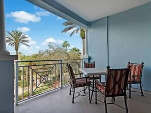 A balcony with a table and chairs, a view of palm trees, and a clear sky. - Pool-View 2BR Condo w/ Hammock Beach Resort Access (Palm Coast)