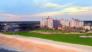 Et stort hotel med flere bygninger, en velholdt golfbane og en strand i forgrunden.