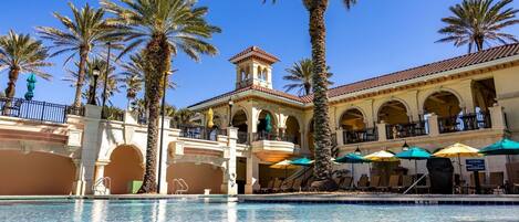 Un hotel con piscina, palmeras y zona de estar exterior con sombrillas.